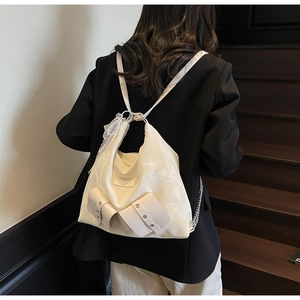 Detail of cream tote bag featuring bow pockets, metallic studs, and delicate lace trim