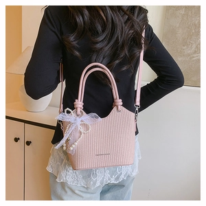 Détail du sac seau rose tressé avec nœud en perles et bandoulière porté par un modèle