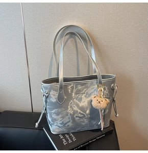 Detail of silver metallic tote bag with logo branding and a cute plush bear charm