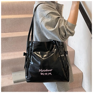 Detail of black patent leather tote bag featuring pink bow embroidery and side ribbon ties