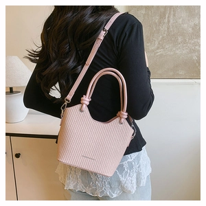 Détail du sac seau tressé rose avec des poignées nouées décoratives et une longue bandoulière