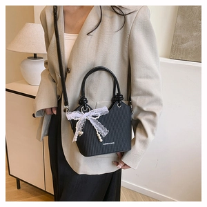 Détail d'un sac seau tissé noir orné d'un nœud en dentelle, de perles et d'un pendentif