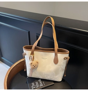 Detail view of cream tote bag with marble pattern, brown PU trim and plush bear charm