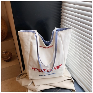 Detailed view of white canvas tote featuring C'EST LA VIE embroidery and blue striped straps