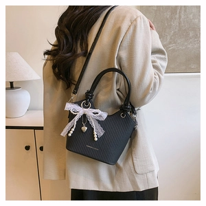 Détail du sac seau noir tissé avec nœud en dentelle et breloque cœur en perles fines