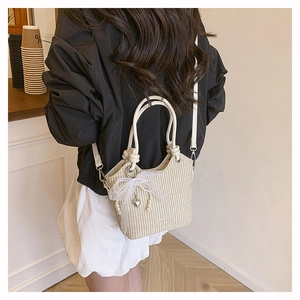 Détail du sac seau en paille beige avec nœud en dentelle, perles et pendentif