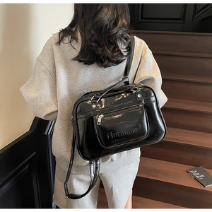 Close-up of black glossy oil wax leather shoulder bag with functional front zipper pocket