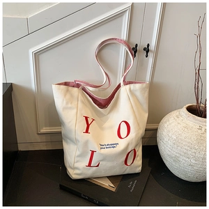 Detail view of canvas tote bag showing red YOLO embroidery and red striped interior lining
