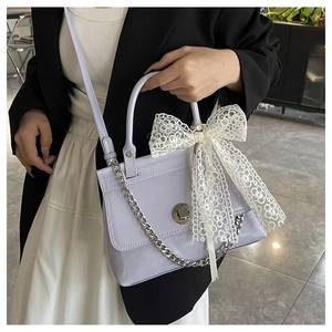 Détail du sac à main lavande en cuir ciré avec nœud en dentelle blanche et chaîne