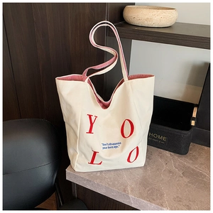 Detail of white canvas tote bag with red YOLO embroidery and striped shoulder straps