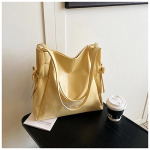 Detail of soft yellow PU leather tote bag with elegant side bow and white embroidery