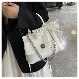 Détail du sac à main blanc avec un grand nœud en dentelle et une bandoulière à chaîne argentée