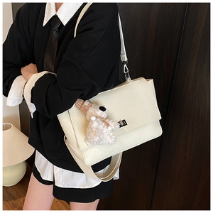 Detail of minimalist beige tote bag with litchi texture and a cute plush bear charm