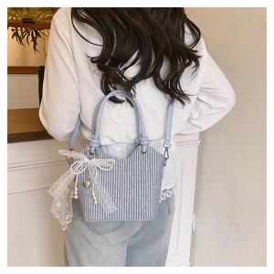 Détail d'un sac seau tressé bleu clair avec nœud en dentelle et breloque en perles