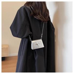 Detail of silver mini crossbody bag with star relief worn on black wool coat
