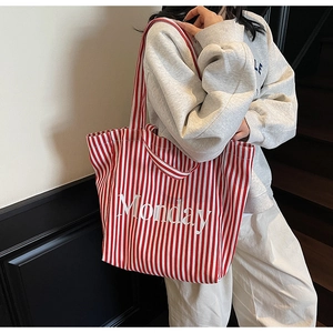 Detail of red and white striped canvas tote bag with Monday text worn by a model