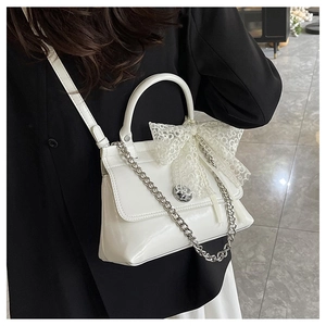 Détail d'un sac à main blanc en cuir brillant avec noeud en dentelle et chaîne argentée