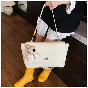 Detail view of cream white leather tote bag with silver lock and plush bear charm decoration