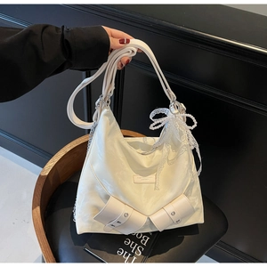 Detail view of cream tote bag with large bows and a pearl butterfly charm on a leather chair