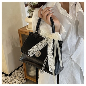 Détail d'un sac bandoulière en cuir noir avec nœud en dentelle blanche et fermoir argent