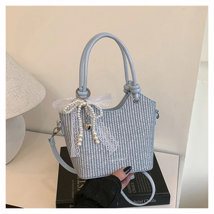 Détail d'un sac seau tissé bleu clair avec un nœud en perles et une bandoulière en cuir