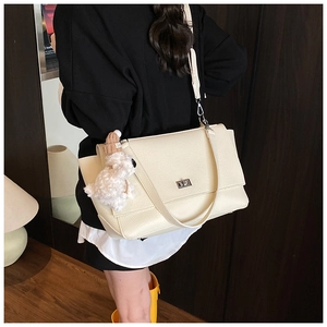 Detail view of cream lychee texture leather shoulder bag with metallic twist lock and plush charm