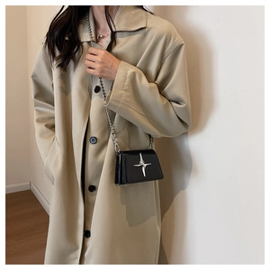 Mini black leather crossbody bag with silver star accent worn over a khaki trench coat