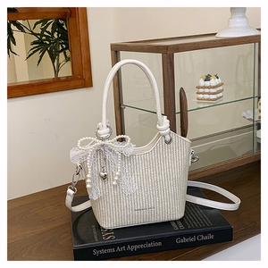 Détail du sac seau en paille crème avec un nœud en dentelle et un charme en perles