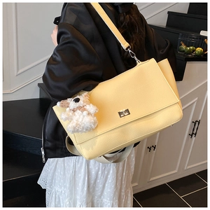 Detail of yellow pebbled leather shoulder bag with silver turn lock and plush dog charm
