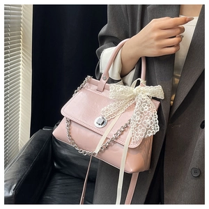 Détail d'un sac à main rose en cuir brillant avec nœud en dentelle et chaîne argent