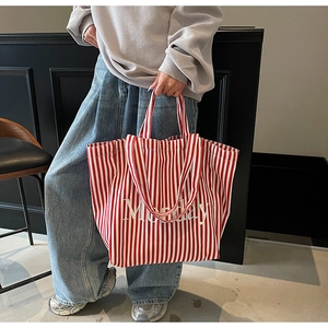 Detail of red and white striped canvas tote bag with Monday print held by a model