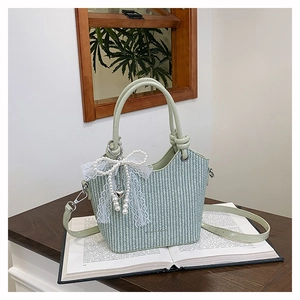 Détail du sac seau tissé vert clair avec nœud en dentelle perlée et pendentif en cœur