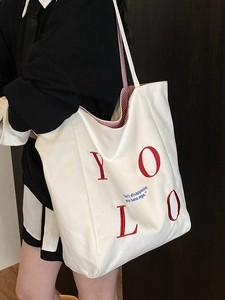 Minimalist white canvas tote bag with red YOLO embroidery and blue inspirational text