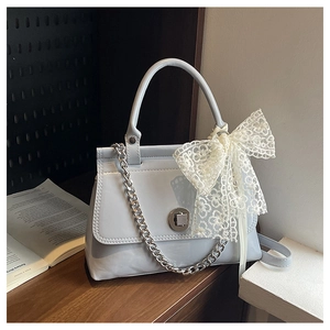 Détail d'un sac à main bleu clair en cuir verni avec chaîne argentée et nœud en dentelle