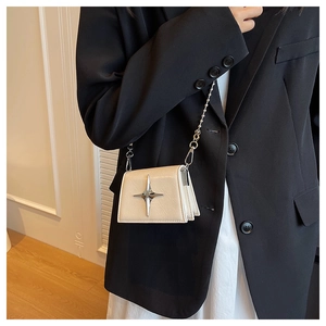Detail of a creamy white mini crossbody lipstick bag with silver star and bead chain