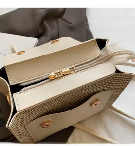 Detail view of cream leather and straw woven bag featuring gold zipper and magnetic closure