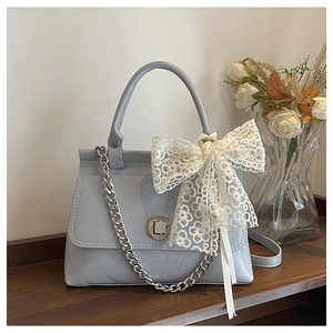 Détail du sac en cuir verni bleu clair avec nœud en dentelle et chaîne argentée