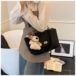 Detail view of black leather briefcase bag with silver twist lock and teddy bear charm