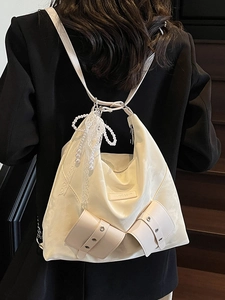 Cream satin tote bag with pearl lace bow charm worn by a model in a black suit