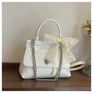 Détail d'un sac à main blanc verni avec nœud en dentelle et bandoulière chaîne argentée