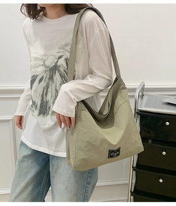 Detail view of large olive green nylon tote bag featuring side pocket and brand label