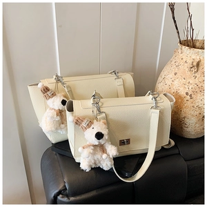 Detail of cream lychee texture handbag featuring silver twist lock and plush puppy charm