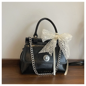 Détail d'un sac à main en cuir verni noir avec chaîne argentée et nœud en dentelle blanche