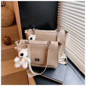 Close-up of beige lychee grain leather handbag with metal turn-lock and plush bear charm