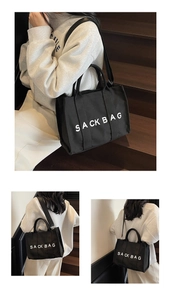 Detail of a black canvas SACK BAG tote featuring white letters and adjustable strap