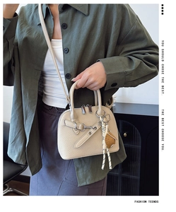Detail of a cream shell-shaped handbag with lychee texture and woven rope charm accessories