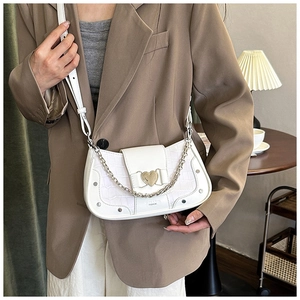 Macro shot of white crocodile-patterned bag with golden heart buckle and silver chain detail