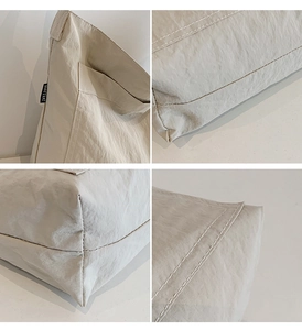 Detail showing the white double stitching and black brand label on the cream tote bag