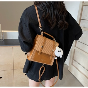 Detail of brown woven faux leather bag with golden hardware and white plush keychain
