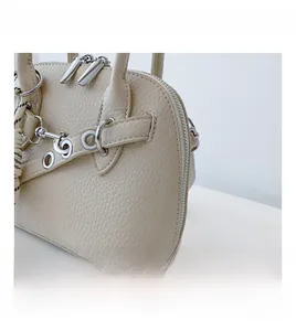 Close-up of beige lychee grain shell bag with silver zipper and striped scarf detail